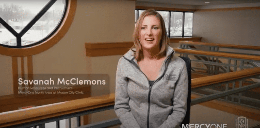 A woman wearing a light gray jacket sits on a bench and smiles at the camera. Text on the image reads: "Savanah McClemons, Human Resources and Recruitment, MercyOne North Iowa at Mason City Clinic." A MercyOne logo is in the bottom right corner.
