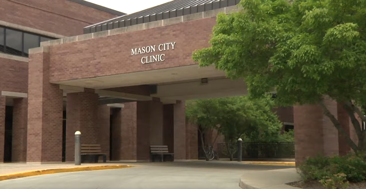 The entrance of Mason City Clinic, a brick building with a covered driveway and two benches, serves as a welcoming gateway to specialized care. Green trees and landscaping surround the area. "Mason City Clinic" is prominently displayed above the entrance, reflecting its role as a specialty clinic in Albert Lea.