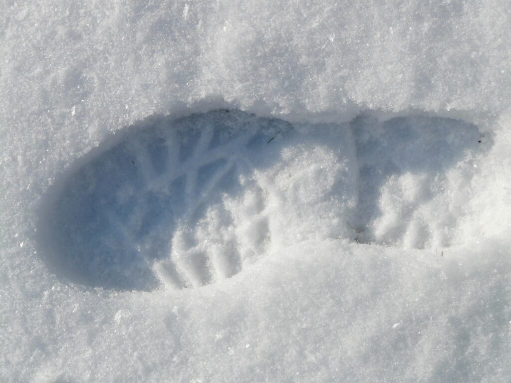 A single shoe print with a distinctive tread pattern is pressed into fresh, white snow. The imprint shows detailed grooves and texture, suggesting a standard outdoor shoe or boot. The surrounding area is untouched.