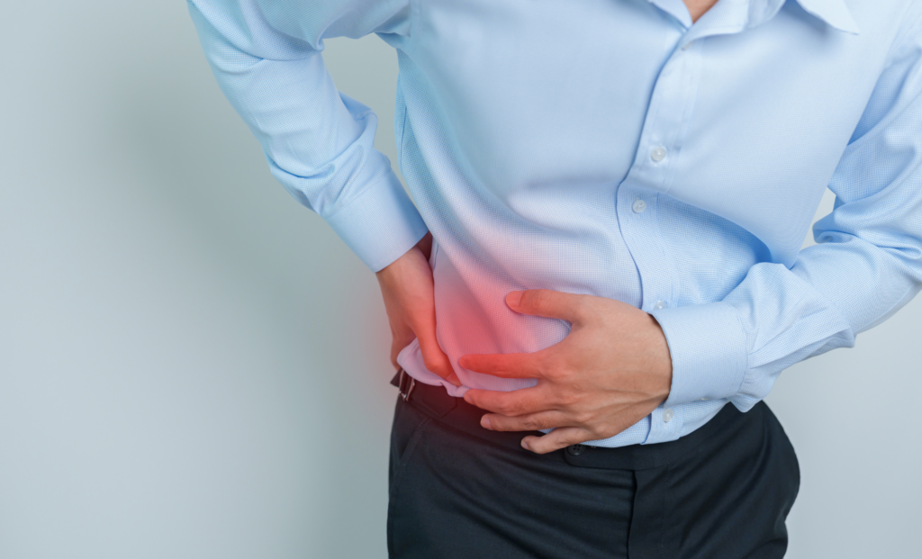 A person wearing a light blue shirt and black pants is clutching their side and lower abdomen, with a red highlight indicating pain or discomfort in the area.
