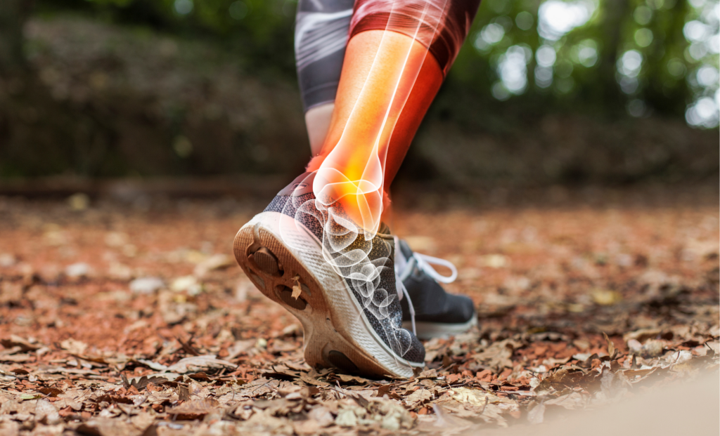 A person walking on a leaf-covered trail in athletic shoes with an illustration highlighting pain or injury in their ankle, shown by glowing and spiral graphic effects around the joint.